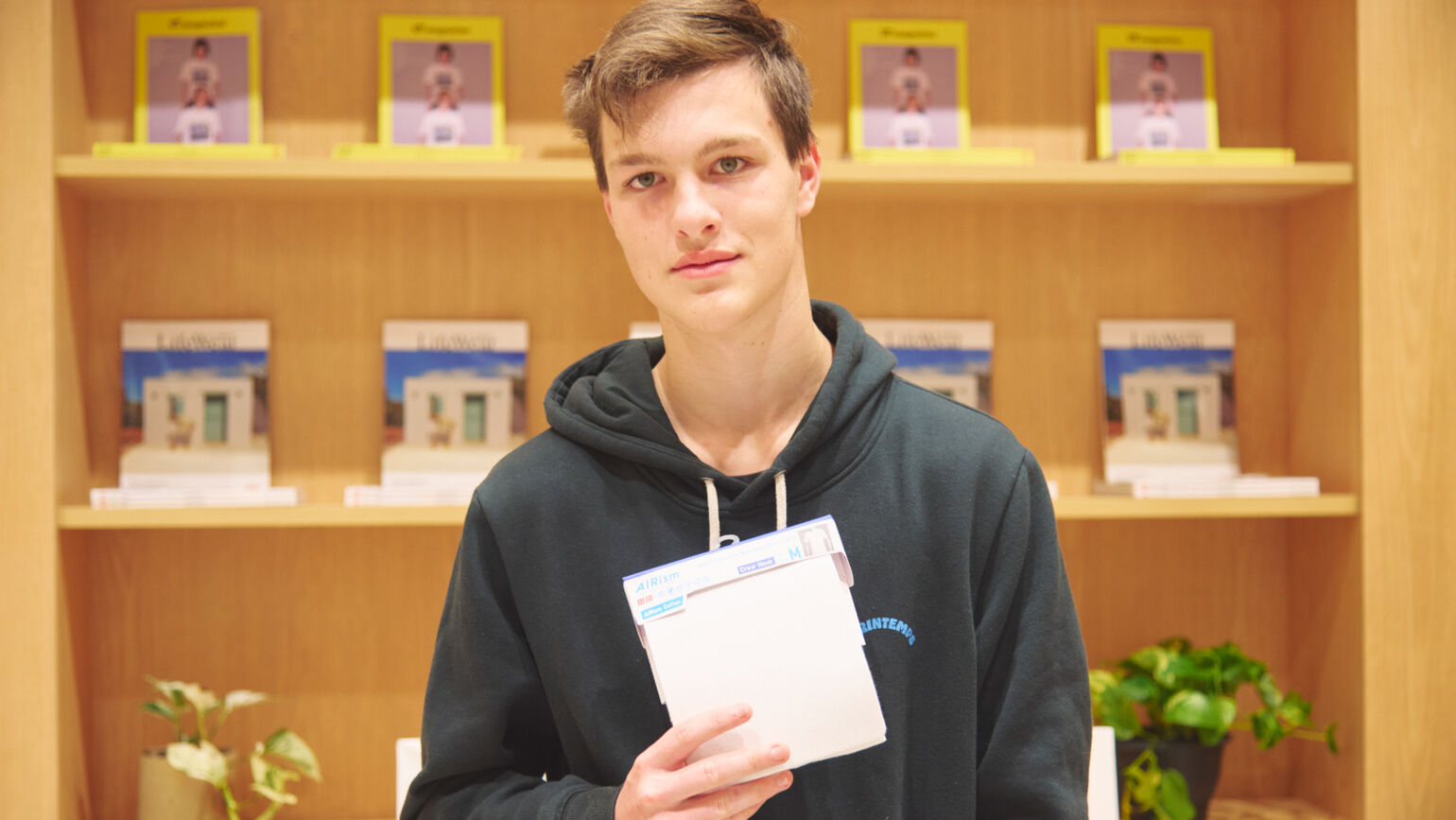 An image of a boy standing in front of a bookshelf, holding a newly received AIRism package carefully with both hands.