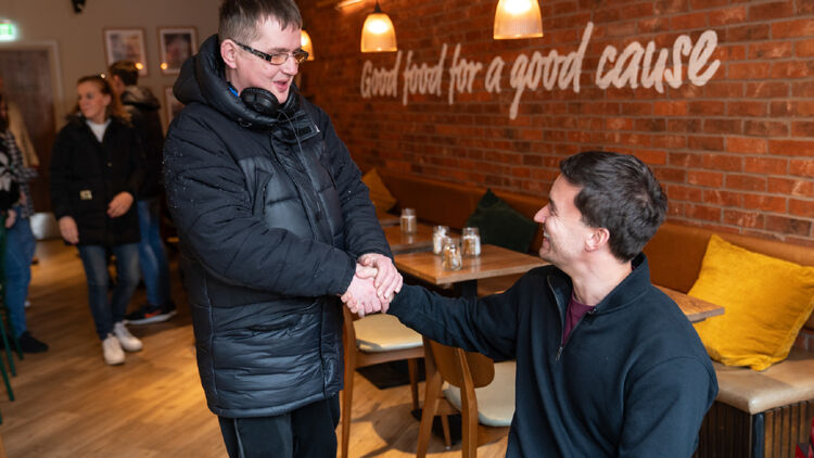 Een afbeelding van Gordon Reid die een man met een bril de hand schudt.