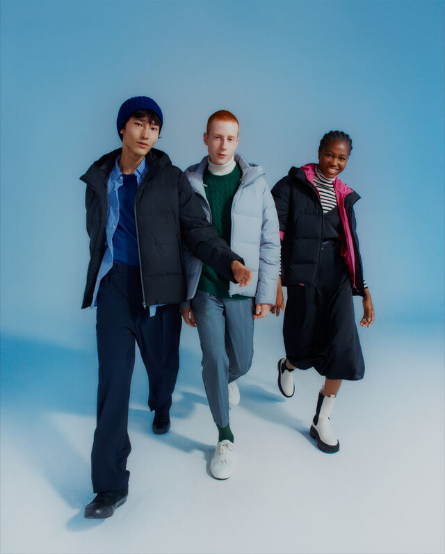 Drei Personen tragen winterliche Outfits mit Daunenjacken in blauen Farben.