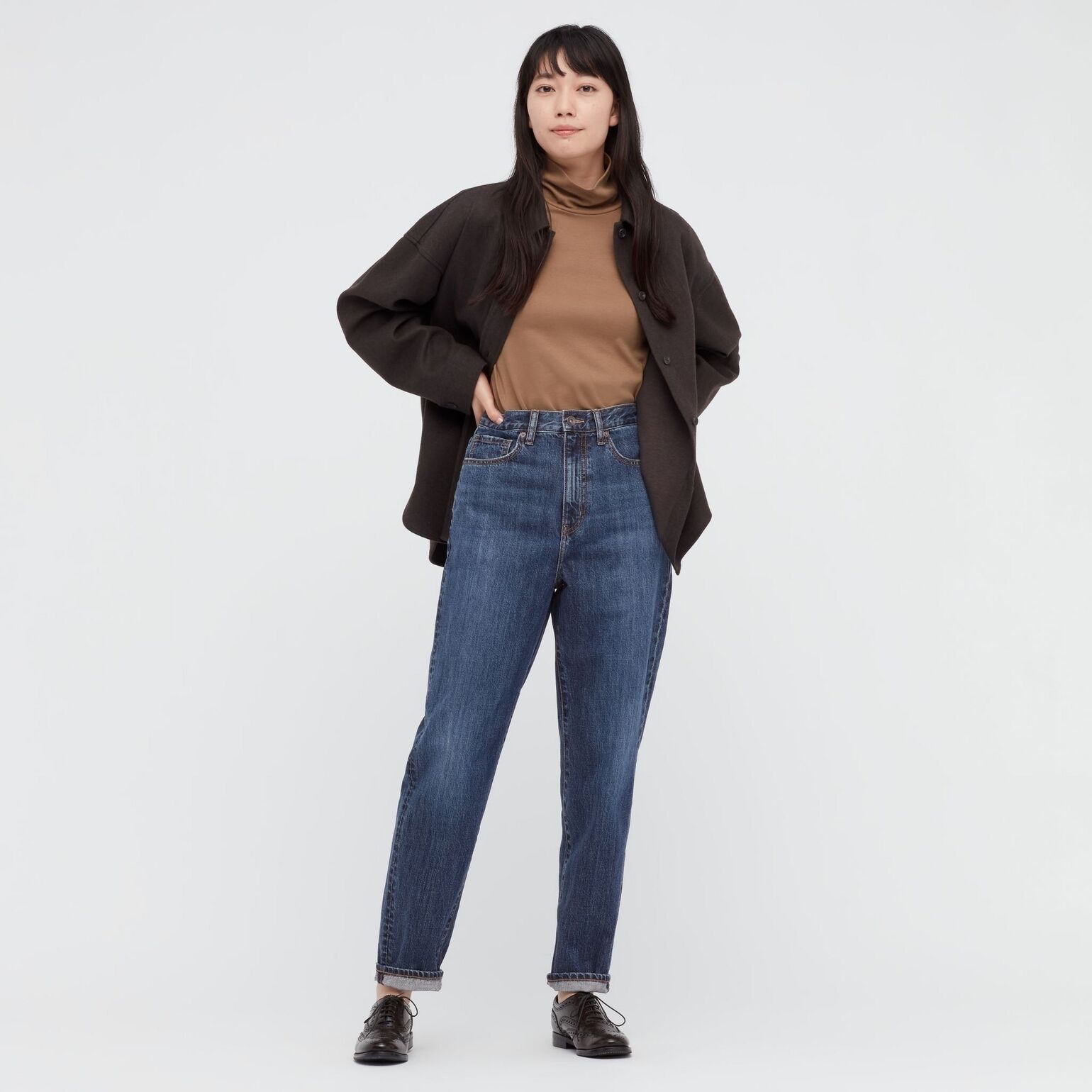 Frau trägt UNIQLO High Waisted Jeans, braunen Rollkragenpullover und braune Strickjacke