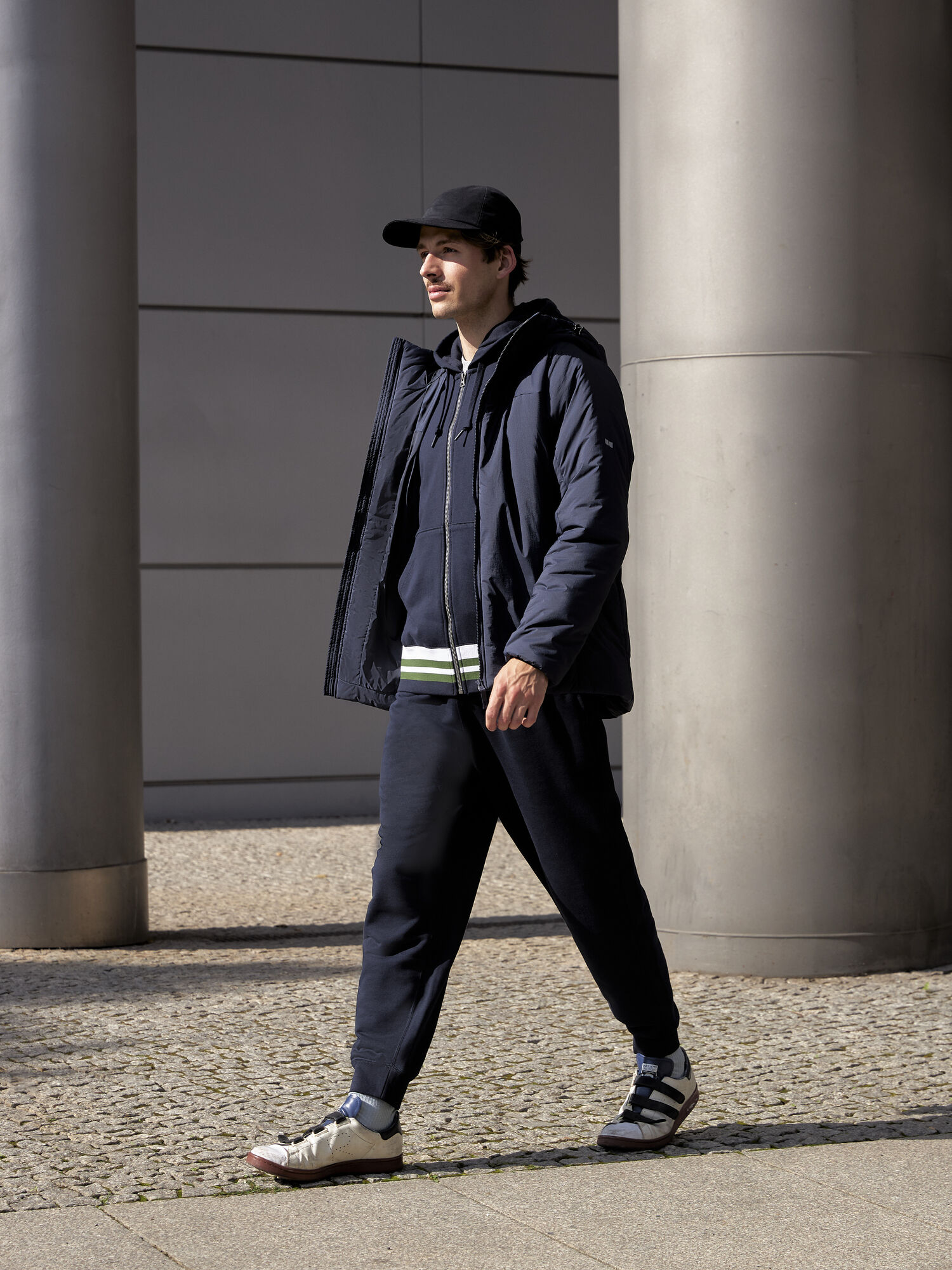 Model trägt dunkelblaue Sweatjacke, Daunenjacke und Jogginghose