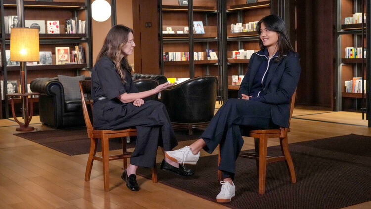 Clare Waight Keller and Emma Raducanu in conversation while sat on wooden chairs