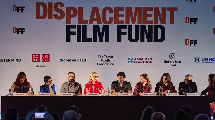 An image of Cate Blanchett and other representatives sitting in a row at a press conference, speaking through microphones.