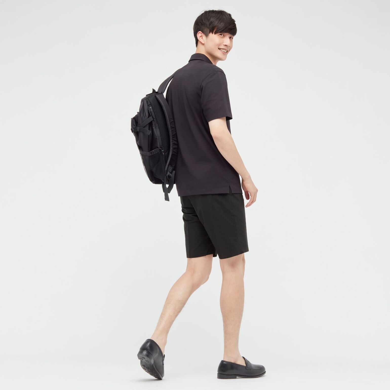 man wearing UNIQLO black polo shirt, black shorts, black backpack, and black loafers