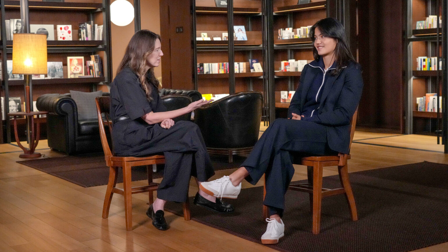 Clare Waight Keller and Emma Raducanu in conversation while sat on wooden chairs