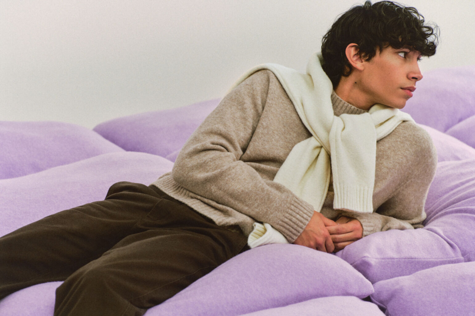 le mannequin est allongé sur un coussin géant et porte un pull en maille Soufflée Yarn, avec un deuxième noué autour des épaules