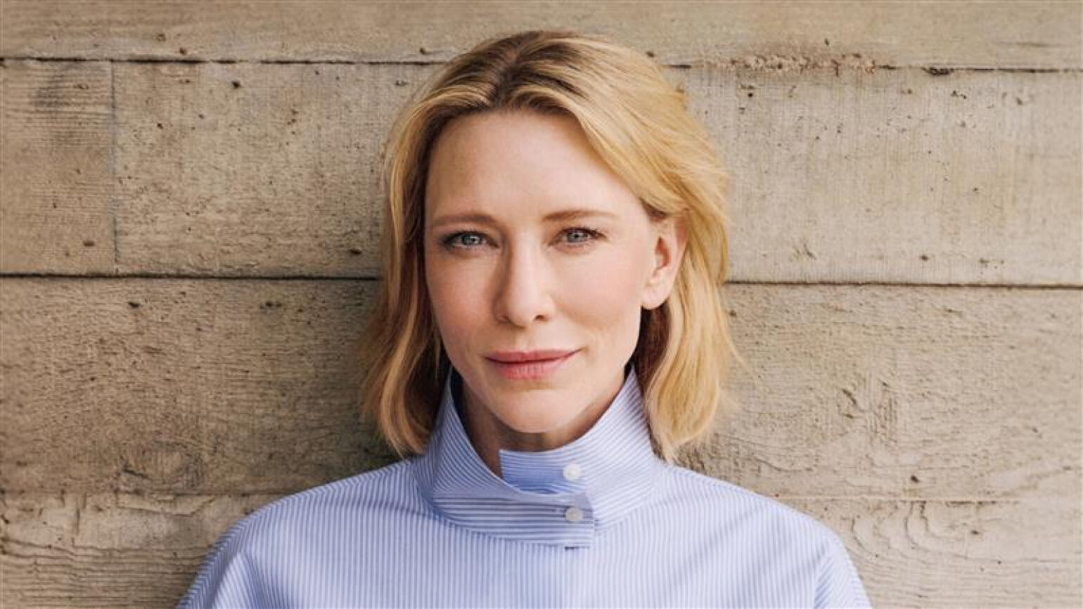 Cate Blanchett sourit à la caméra, dans une chemise à col montant rayée bleu et blanc