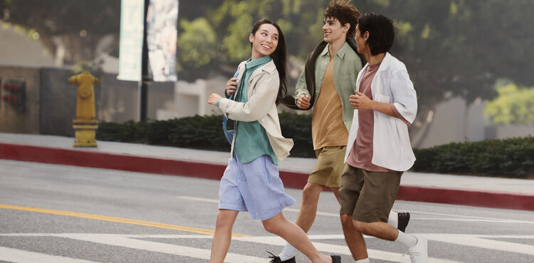 A dynamic image of three people wearing light linen clothing, walking briskly with smiles on a city street abroad.