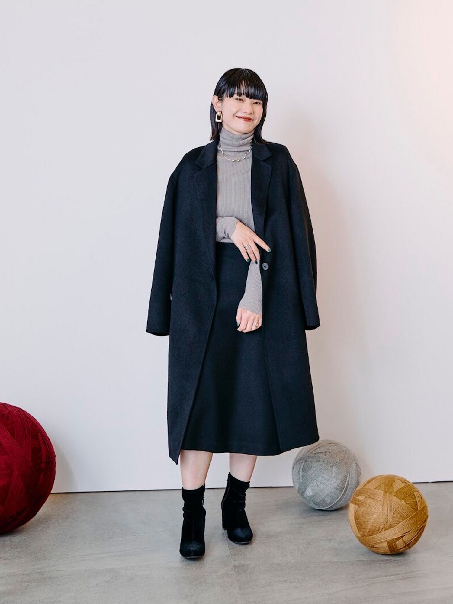 ウール素材のミディ丈スカートに、グレーのリブタートルネック、黒のロングコートを合わせたレディースのブラックコーデ。
