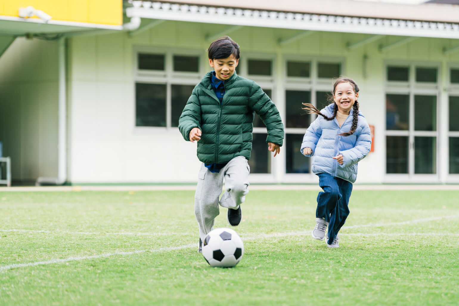 パフテックウォッシャブルパーカ、フランネルチェックシャツ、ドライスウェットカーゴパンツを来てボールを蹴る男の子と、パフテックウォッシャブルパーカ、スフレヤーンセーター、ワイドフィットストレートジーンズを着て走る女の子の画像