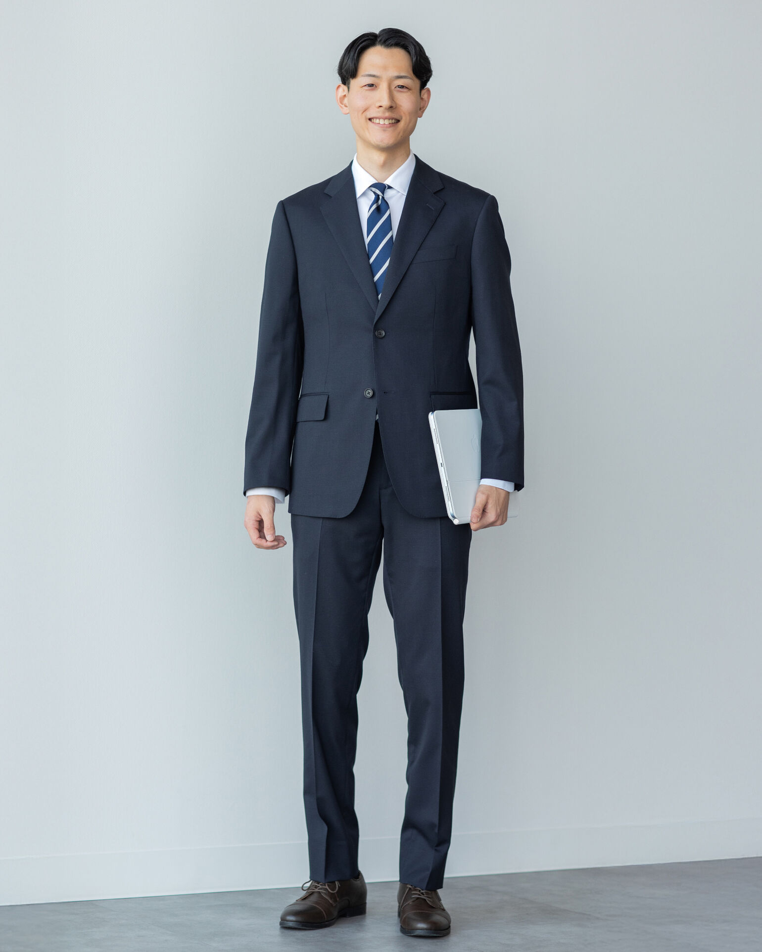 パソコンを持ってこちらを見つめるスーツを着たKentoさんの画像