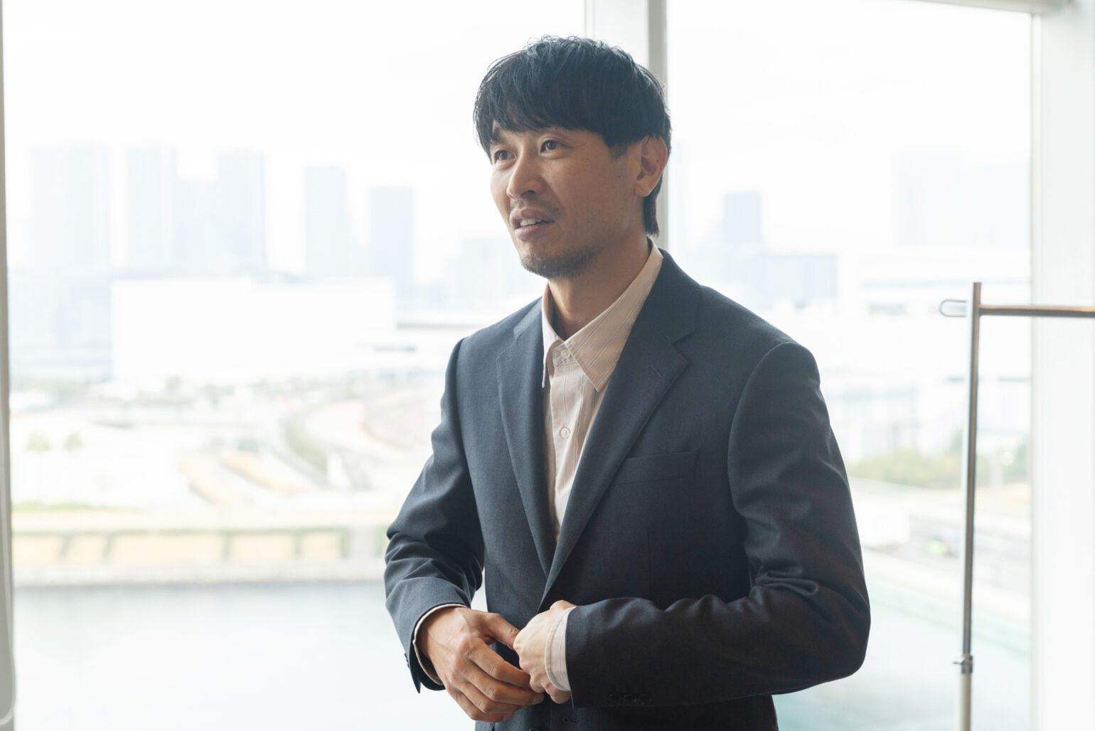 スーツのボタンを触りながらこちらを見ている男性の画像