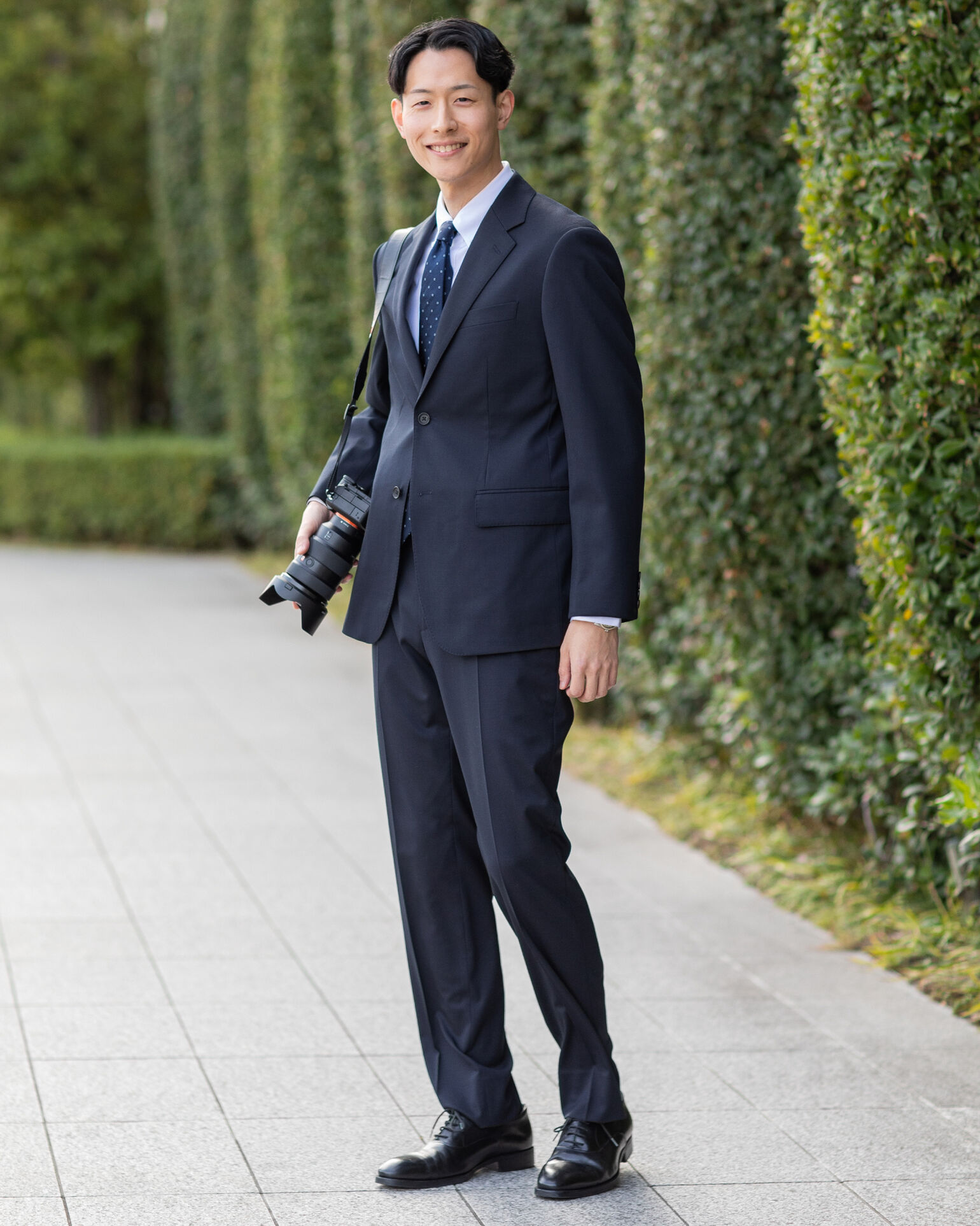 カメラを持ってこちらを見つめるスーツを着たKentoさんの画像