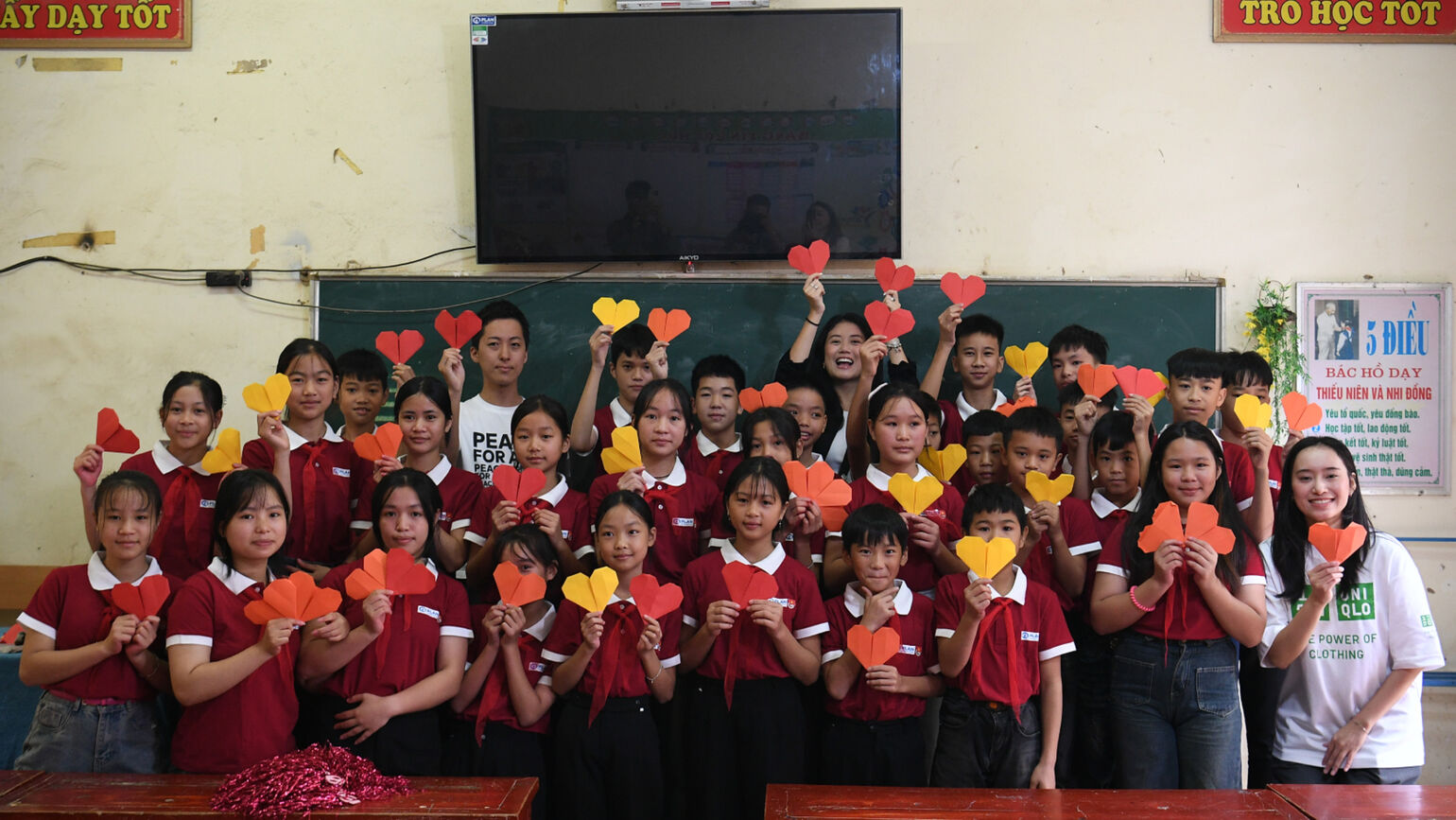 教室にて、子供たちが折り紙のハートを掲げて笑顔で見つめる集合写真の画像