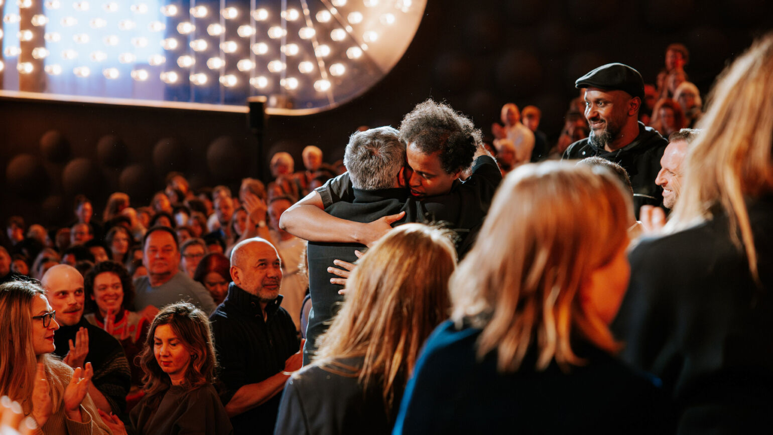 映画祭の会場で、二人の男性が力強く抱き合っている感動的な瞬間の画像。