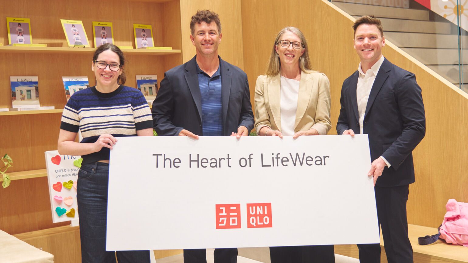 店内の階段を背景に、アダム・スコット選手含む4名の関係者が「The Heart of LifeWear」と大きく書かれた白いボードを一緒に持っている集合写真の画像。