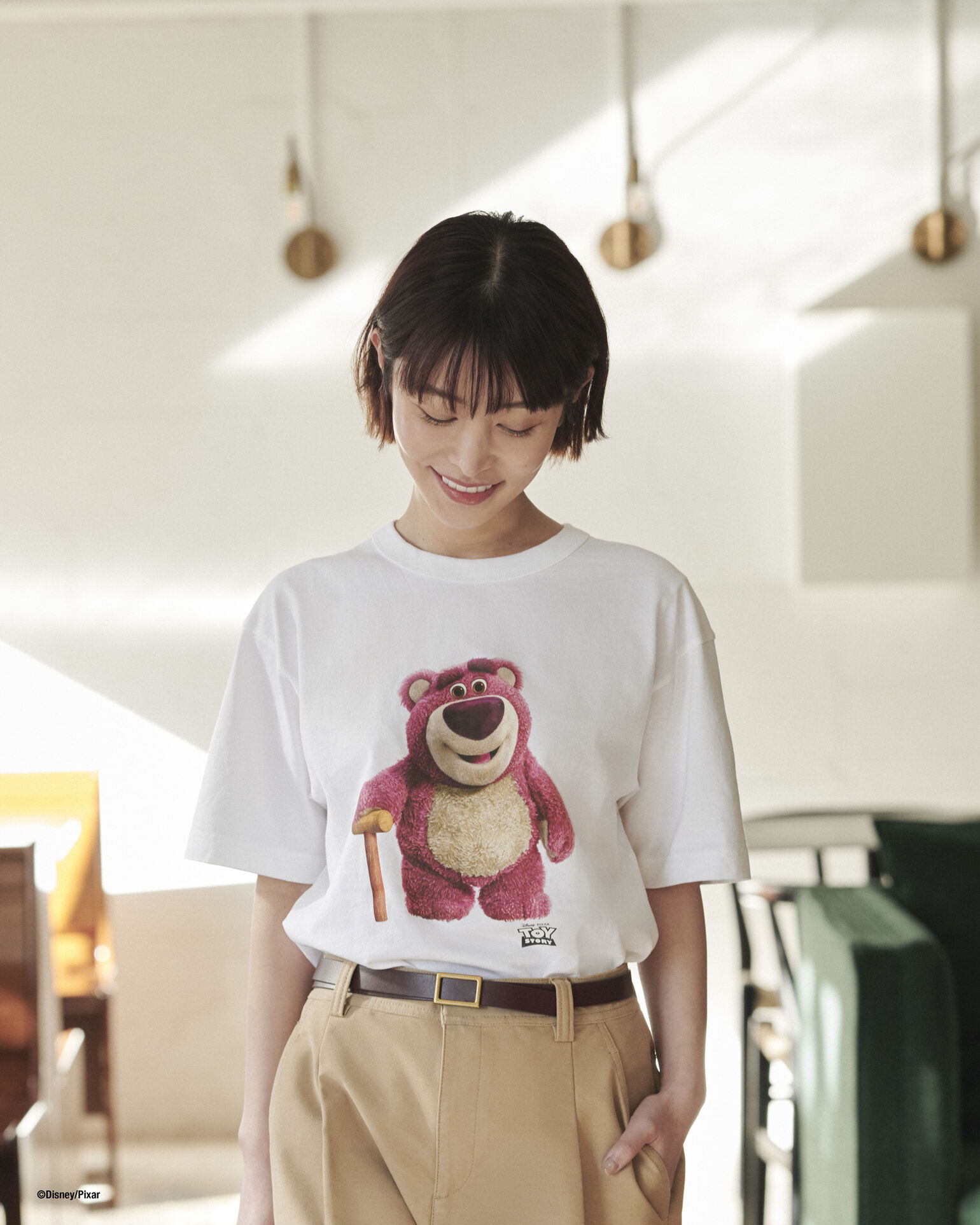 トイ・ストーリーの「ロッツォ」がプリントされた白いTシャツを着たJu!ieさんが、柔らかな光の中で伏し目がちに微笑んでいる画像。