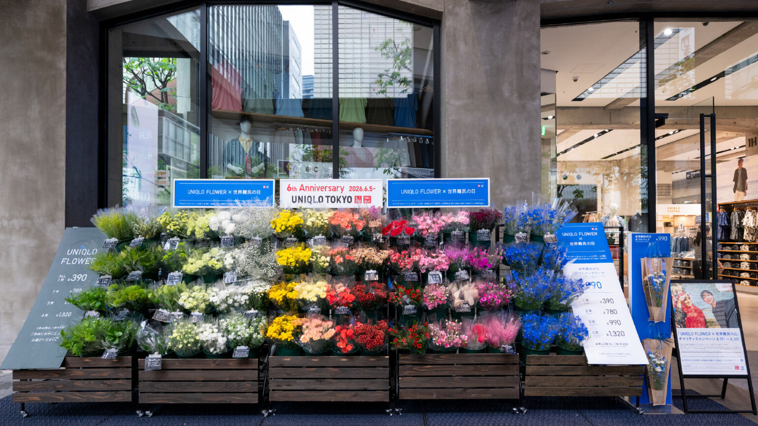 UNIQLO TOKYOの店頭に設置された、色鮮やかなUNIQLO FLOWERの特設売り場。「UNIQLO FLOWER × 世界難民の日」のブルーの看板や、キャンペーンの案内看板が並んでいる。