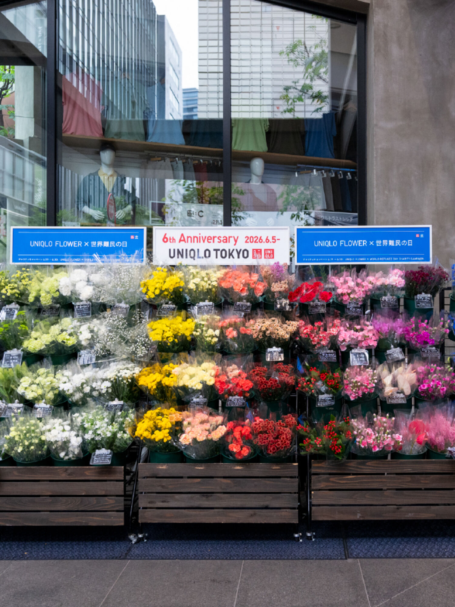 UNIQLO TOKYOの店頭に設置された、色鮮やかなUNIQLO FLOWERの特設売り場。「UNIQLO FLOWER × 世界難民の日」のブルーの看板や、キャンペーンの案内看板が並んでいる。