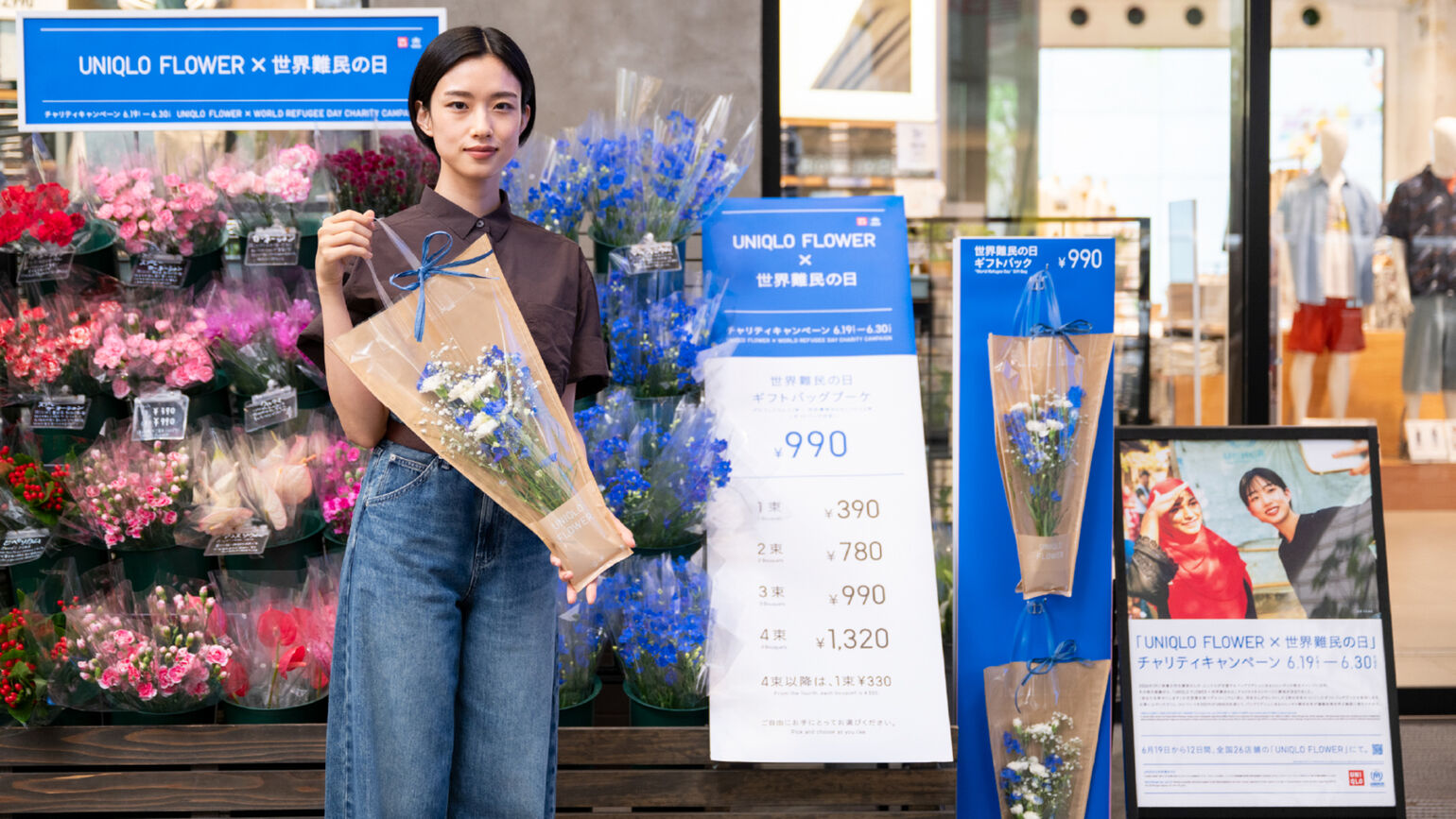 UNIQLO FLOWERの売り場の前で、「世界難民の日ギフトバッグブーケ」を手に持って微笑む俳優の河合優実さん。隣にはキャンペーンの価格表やポスターが設置されている。