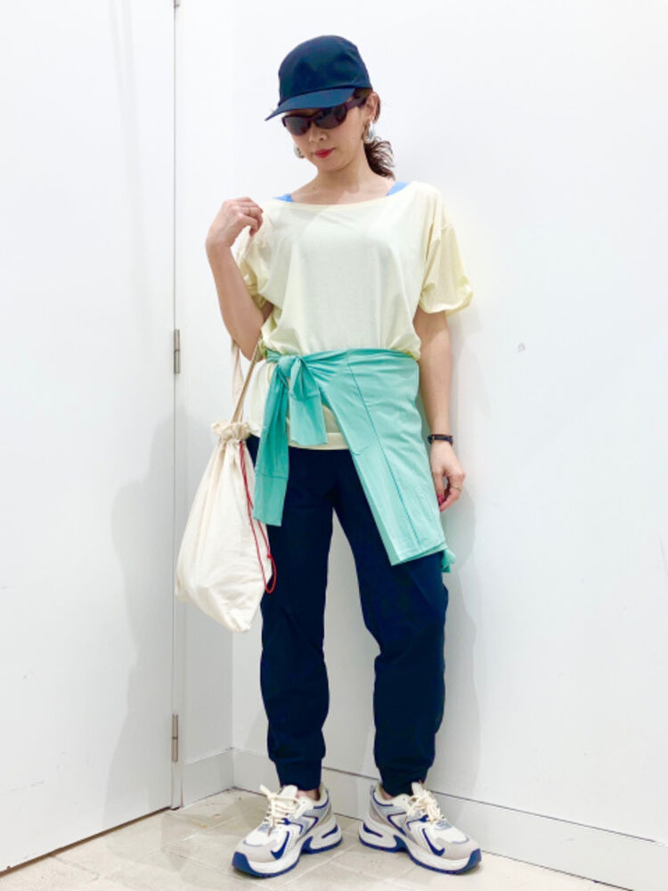 An image of a woman in a full sporty outfit, wearing a navy cap and sunglasses, with a mint green hoodie tied around the waist of a lemon yellow T-shirt.