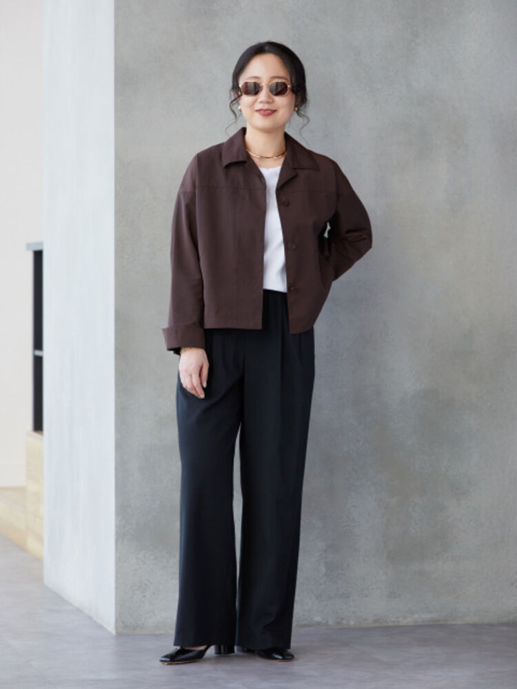 An image of a woman in a chic full outfit, wearing slender polygonal-frame sunglasses, a brown jacket, and black wide-leg pants.