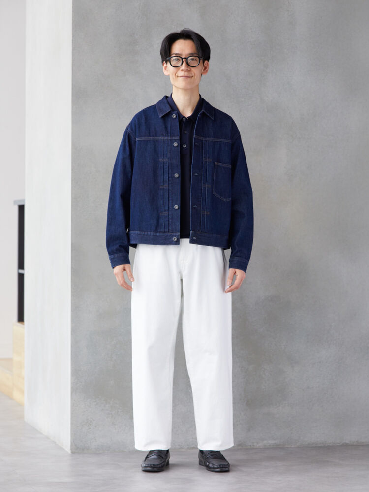 An image of a man in a clean full outfit, wearing black-rimmed glasses, a denim jacket, and white pants.