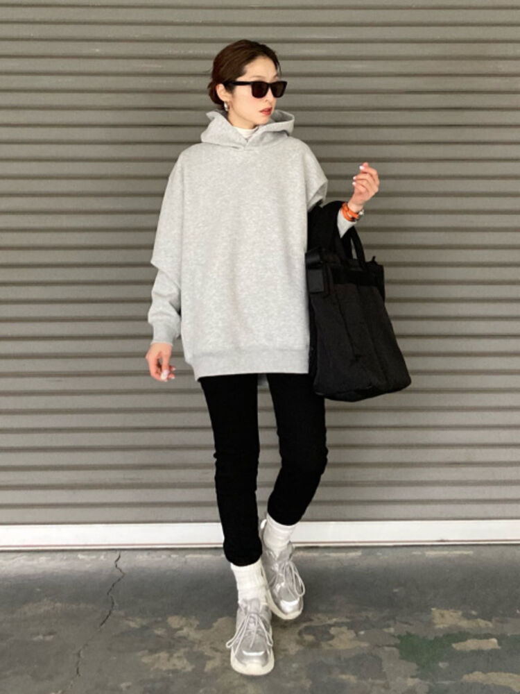 An image of a woman in a full active outfit, wearing black Wellington-style sunglasses, a gray hoodie, black skinny pants, and silver sneakers.