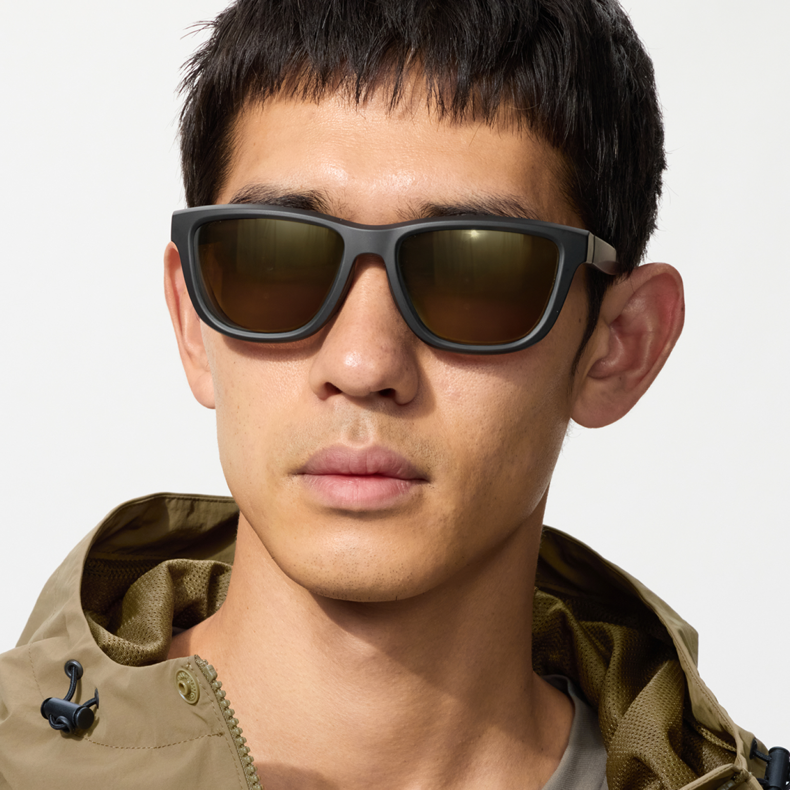 An image of a man in a khaki mountain parka with the hood up, wearing sports square-type sunglasses and looking straight ahead with a powerful gaze.