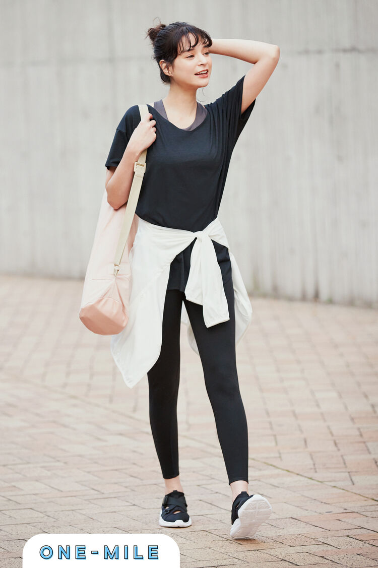 グレーのWワイヤレスブラと黒いエアリズムシームレスＶネックロングＴのレイヤードに黒いレギンスを合わせ腰に白いパーカを巻いた女性