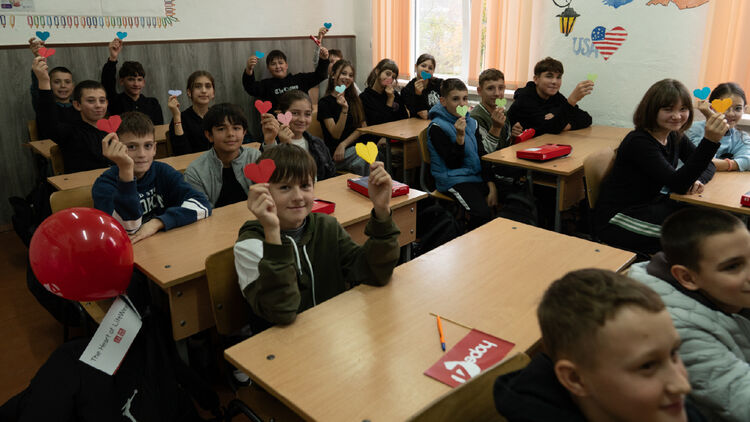 Image of children sitting in a classroom and posing with heart-shaped message cards