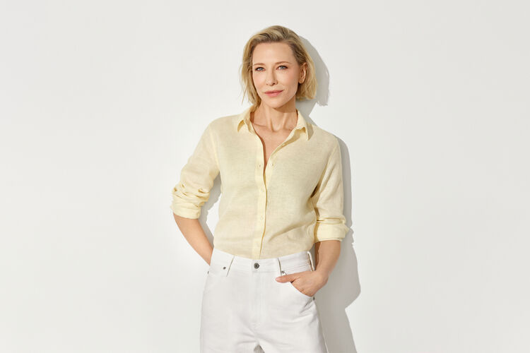 An image of Cate Blanchett standing naturally and looking refreshed, wearing a pale yellow linen shirt paired with white pants.