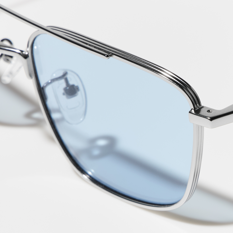 A close-up image capturing the silver frame, light blue lenses, and unique bridge structure of the metal double-bridge sunglasses.