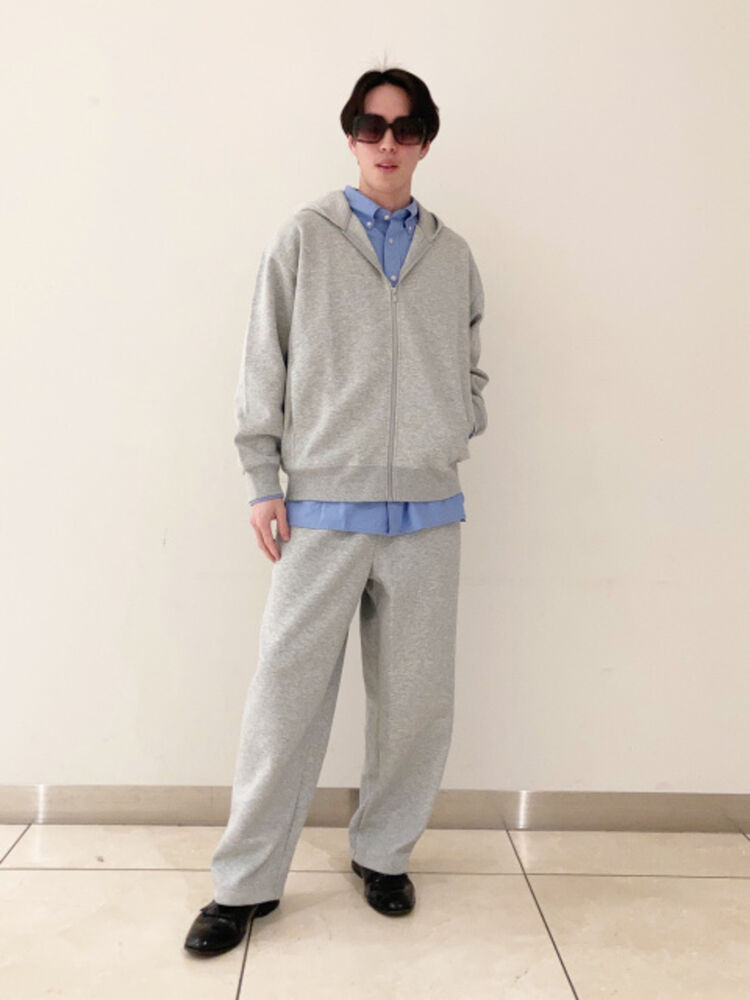 An image of a man in a relaxing full outfit, wearing large square sunglasses, a blue shirt layered over a gray sweatshirt and sweatpants setup.