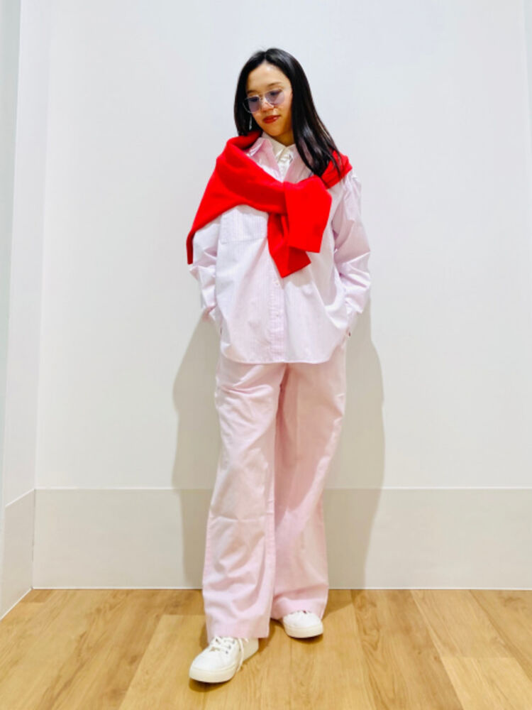 An image of a woman in a glamorous full outfit, wearing light-colored lens sunglasses, a pink striped shirt, and a red knit sweater draped over her shoulders.