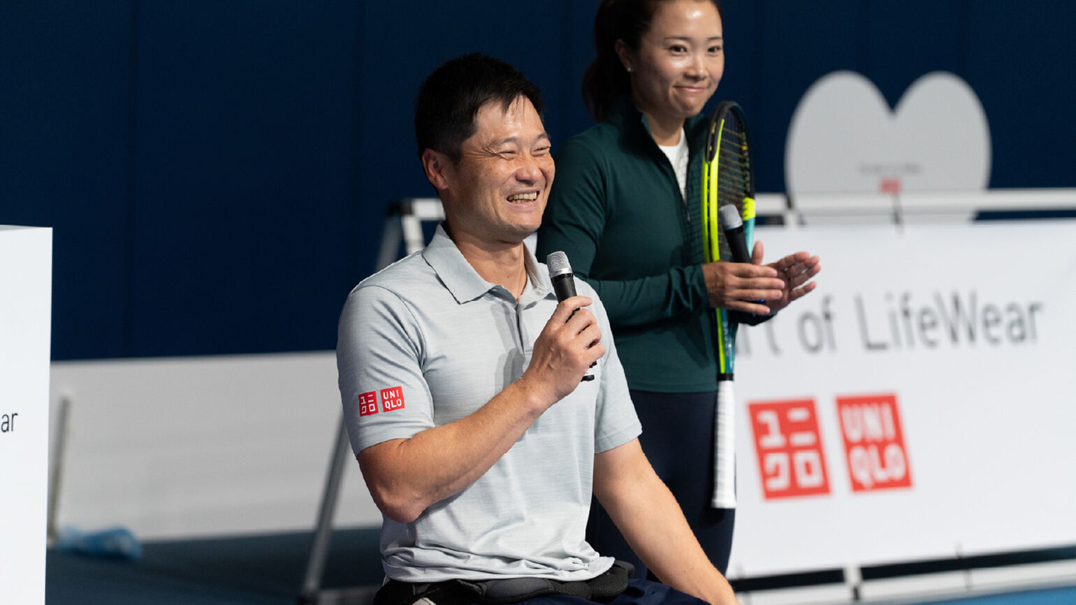 An image of Shingo Kunieda smiling and holding a microphone.