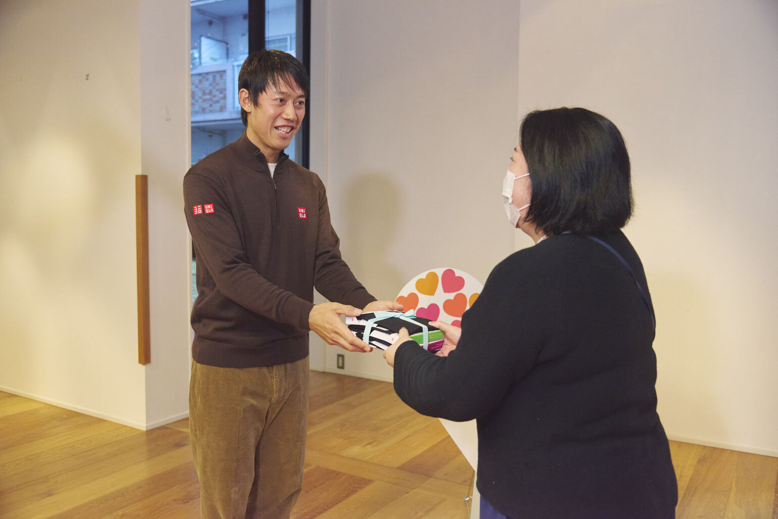 An image of Kei Nishikori smiling and handing a bundle of HEATTECH tied with a ribbon to a woman.