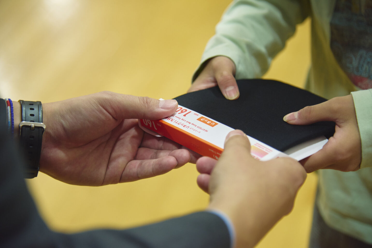 A close-up image of a child in a light green shirt receiving a black HEATTECH package with both hands.