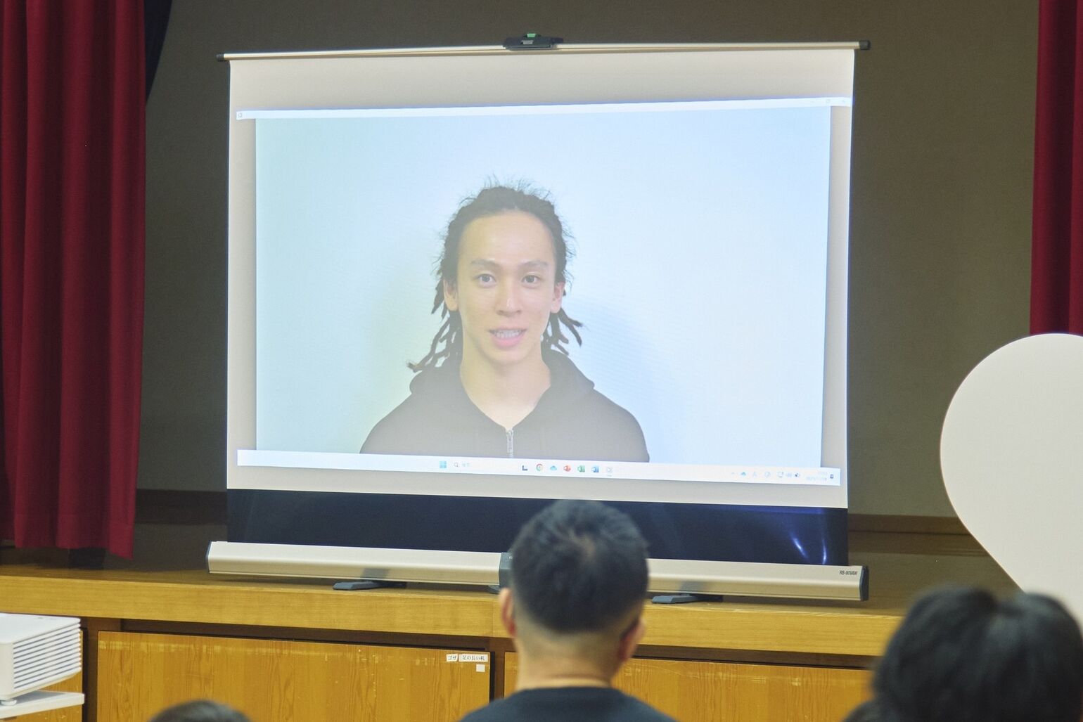 An image of Ayumu Hirano giving a greeting via video message, projected onto a screen.