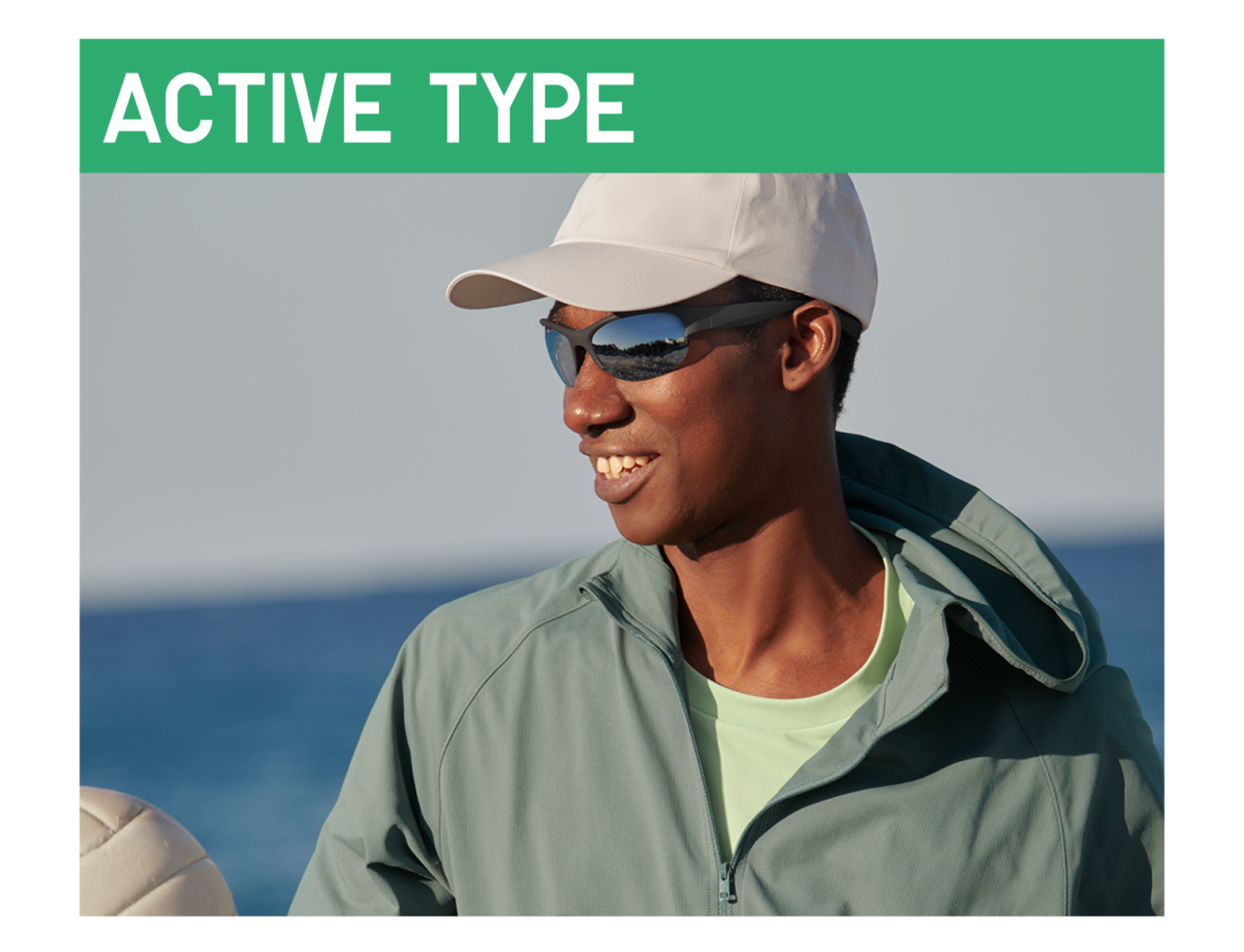 An image of a man wearing sports-type sunglasses and a white cap, smiling against a coastal background under a green 