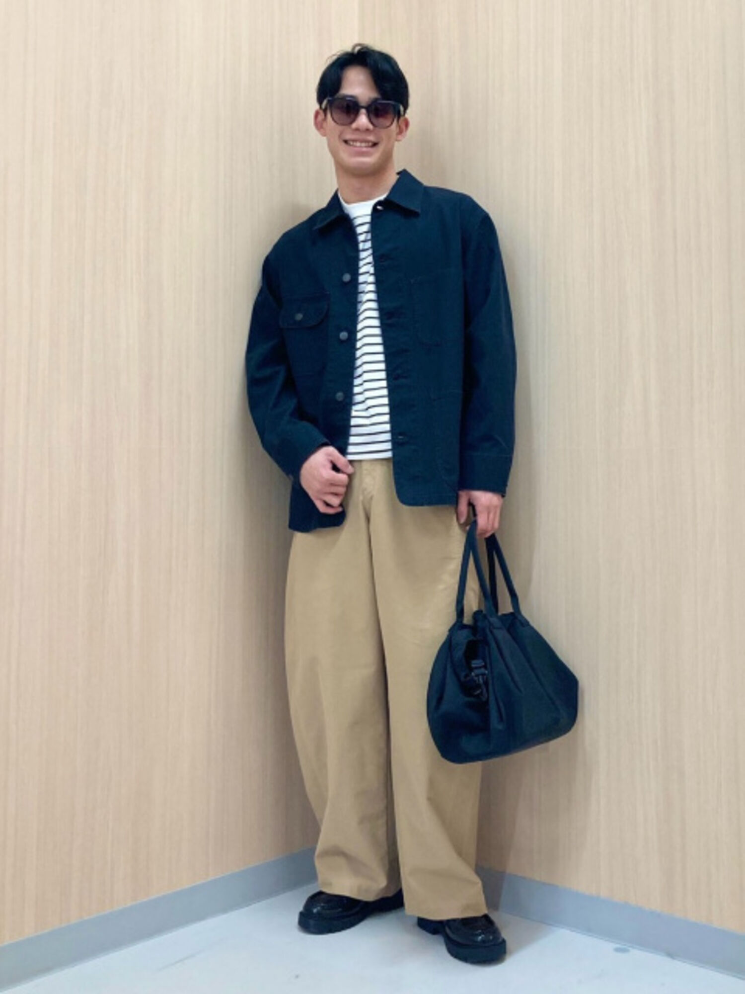 An image of a man in a casual full outfit, wearing slightly tinted square sunglasses, a striped T-shirt, navy coveralls, and beige chino pants.