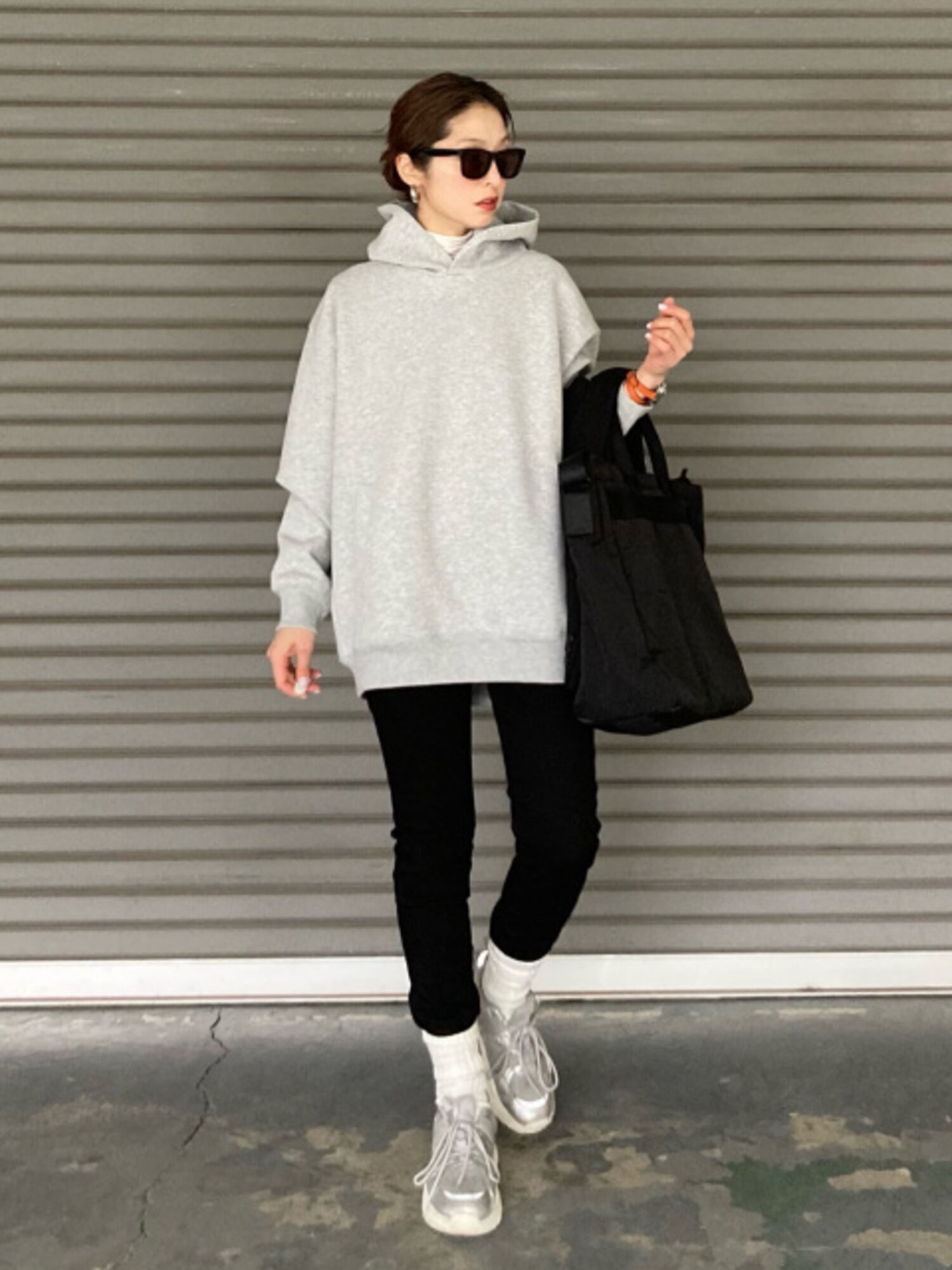 An image of a woman in a full active outfit, wearing black Wellington-style sunglasses, a gray hoodie, black skinny pants, and silver sneakers.