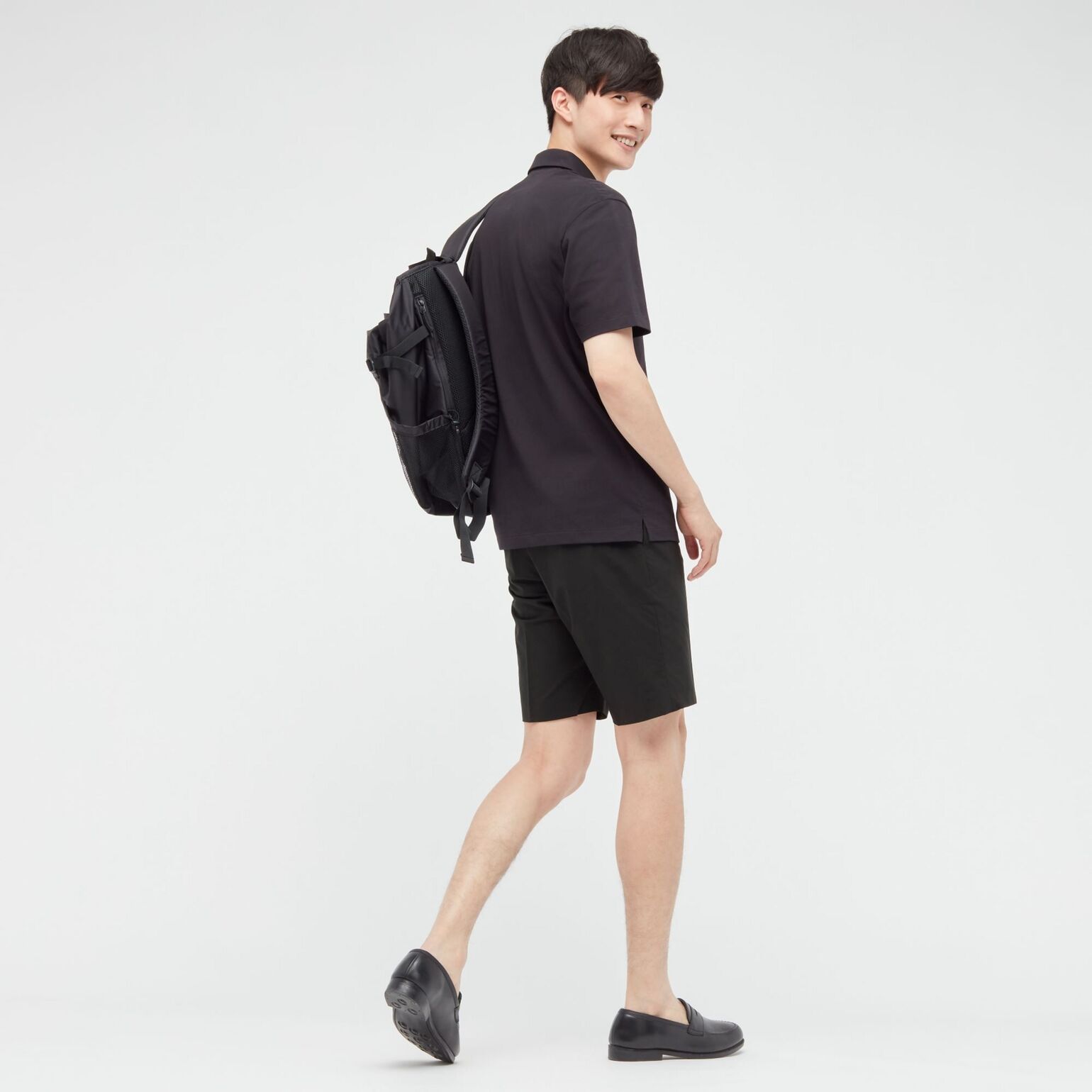 man wearing UNIQLO black polo shirt, black shorts, black backpack, and black loafers