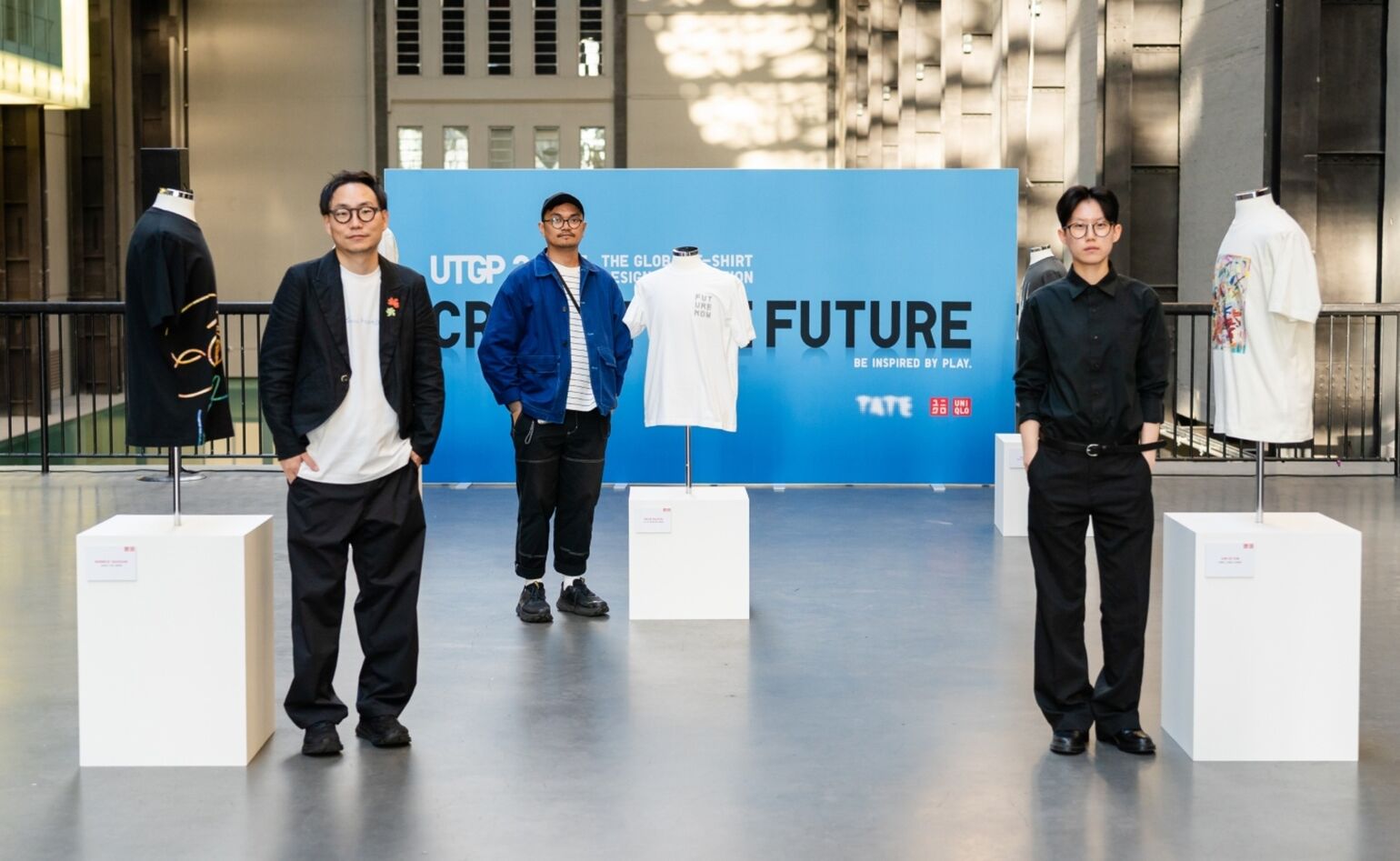 the winners stand next to their winning designs on T-shirts, displayed on mannequins