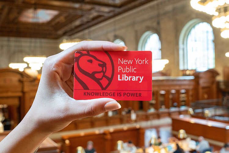 hand holding a New York Public Library card with a lion and text below that says 