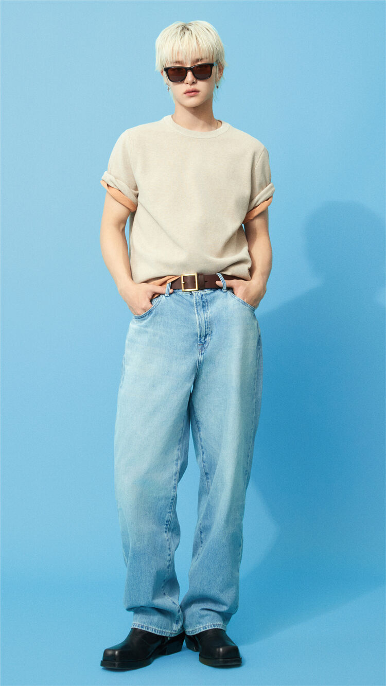 A full-body outfit image of JIHOON standing smartly in a beige knit T-shirt and jeans, wearing foldable Wellington Folding Sunglasses.