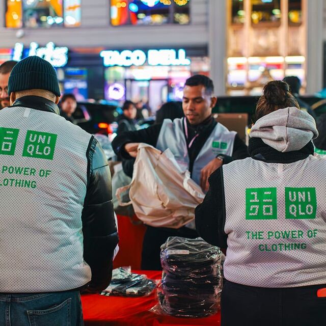 UNIQLO employees volunteer at an evening city event, sorting clothing for community distribution, supporting sustainability initiatives through The Power of Clothing.