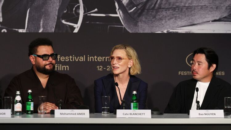 Cate Blanchett (center) speaking into the microphone during the press conference, with Mohammed Amer (left) and Bao Nguyen (right) listening intently by her side.