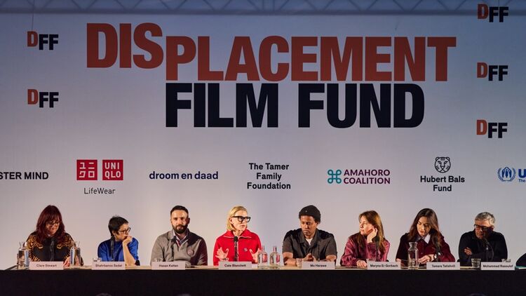 A press conference held in front of a backdrop featuring the large 
