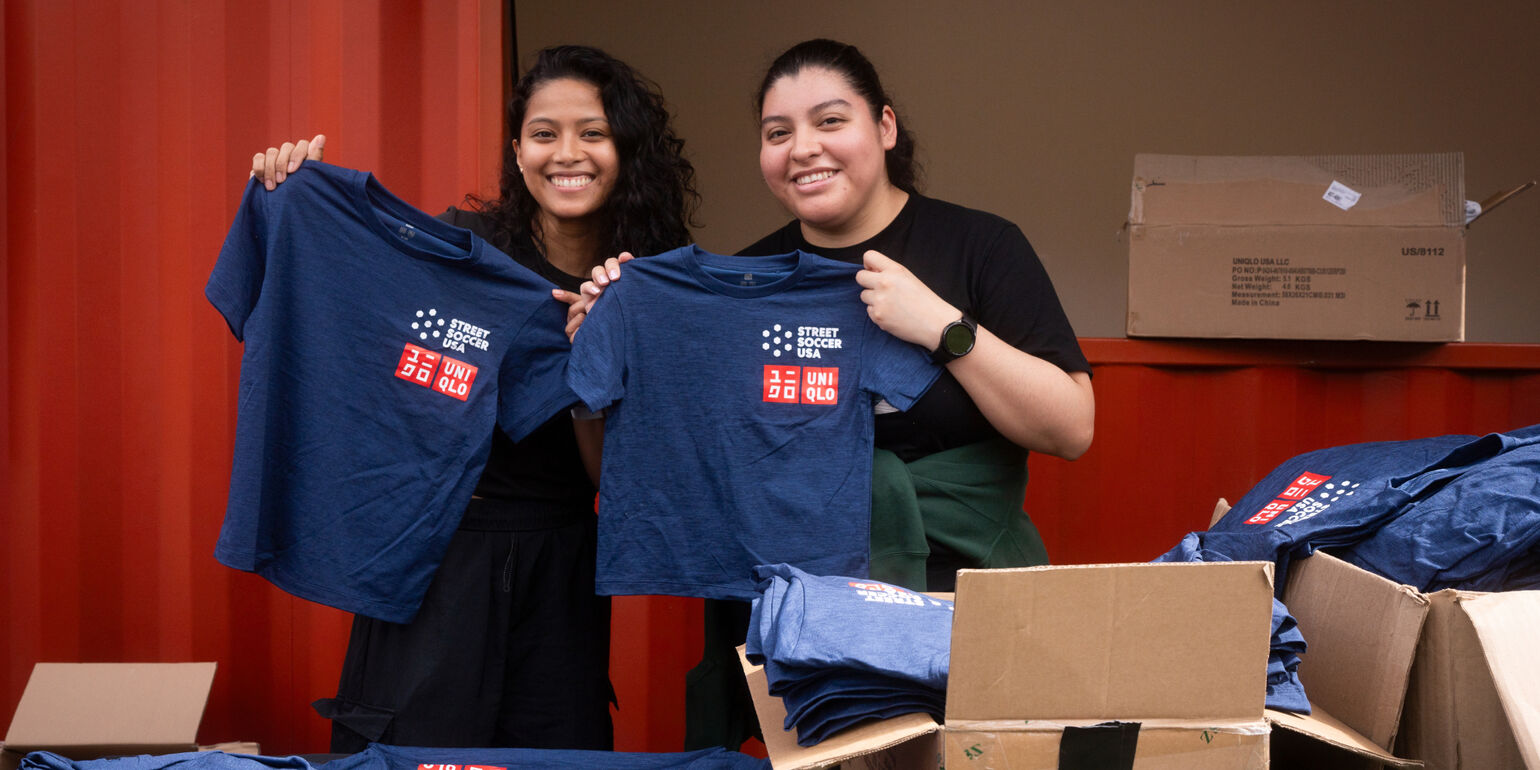 two volunteers holding navy Uniqlo short sleeve shirts at a volunteering event